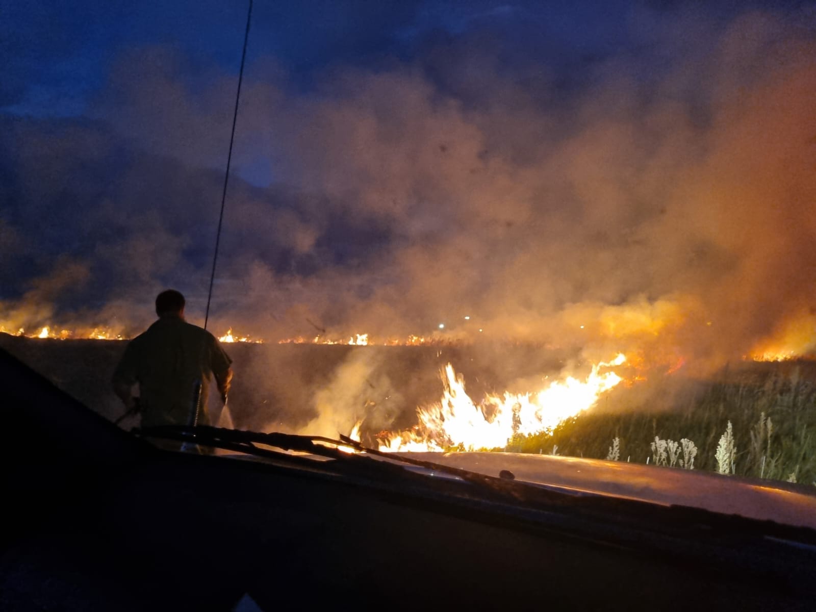 'n Man staan in die voorgrond terwyl die veld brand.